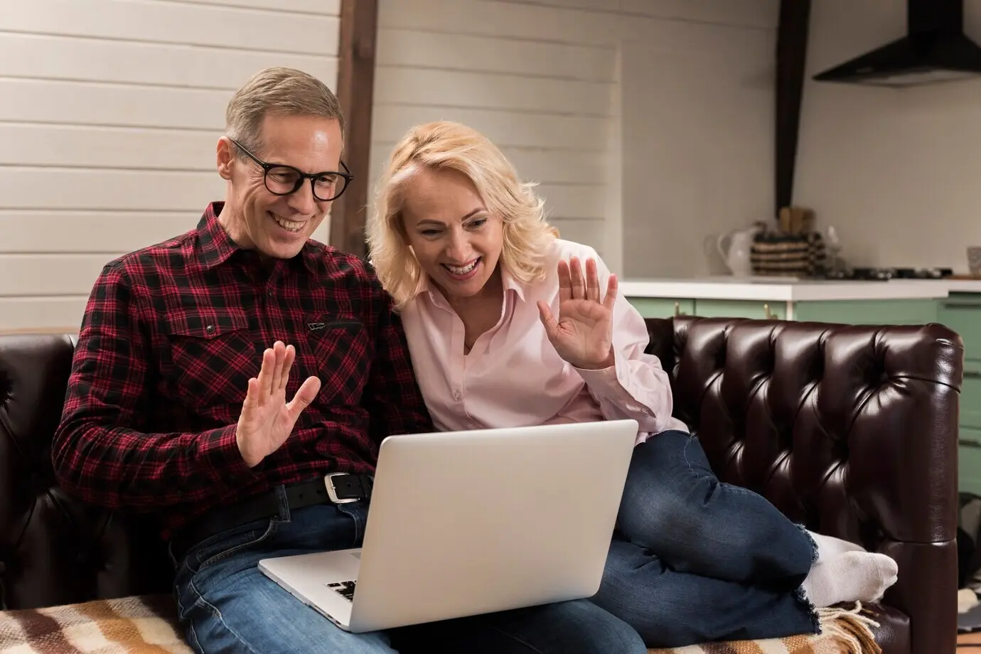 Fröhliche Eltern winken auf dem Sofa einem Laptop zu.